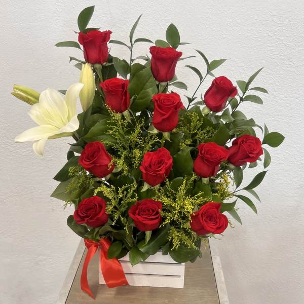 Red roses and white lilies arranged in a white box with a red ribbon