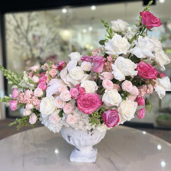 Pink and white rose arrangement in a white pedestal vase