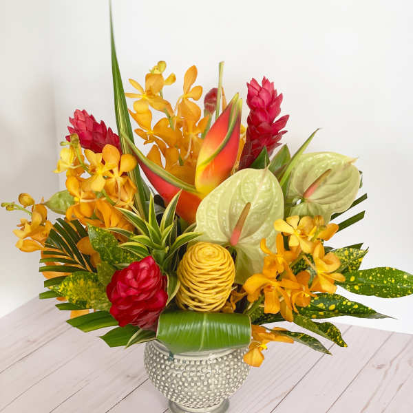 Tropical flower arrangement in a textured silver vase with red, orange, and green blooms