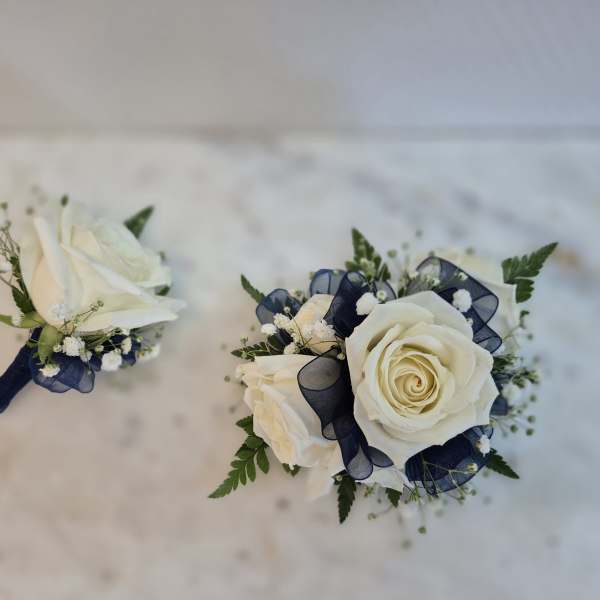 Two white rose boutonnieres with navy ribbon accents