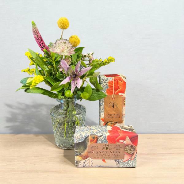 Small mixed flower bouquet in a glass vase beside two boxed soaps