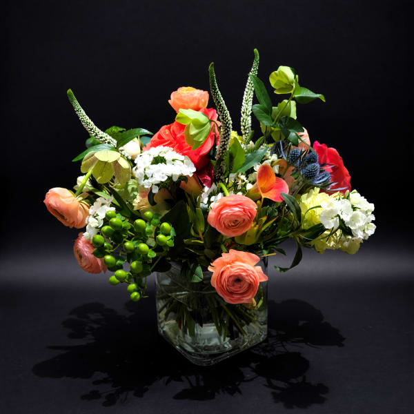 Mixed bouquet of coral, white, and green flowers in a clear glass vase