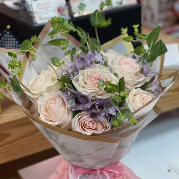 Bouquet of pale pink roses and purple flowers wrapped in paper