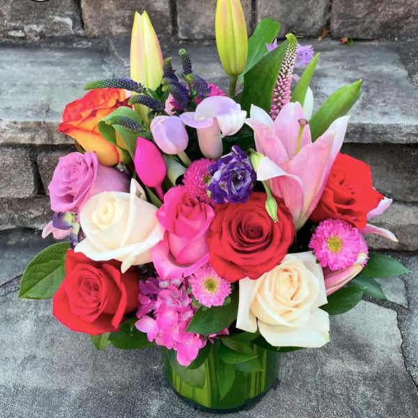 Colorful arrangement of roses, lilies, tulips, and mixed blooms in a clear glass vase