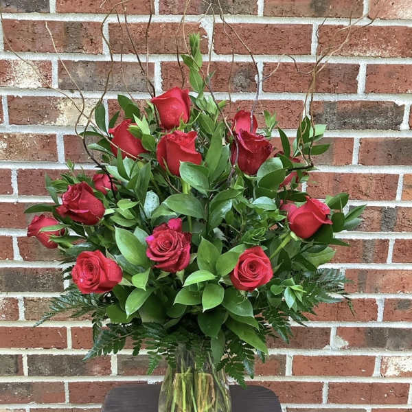 Red roses arranged in a clear glass vase with greenery