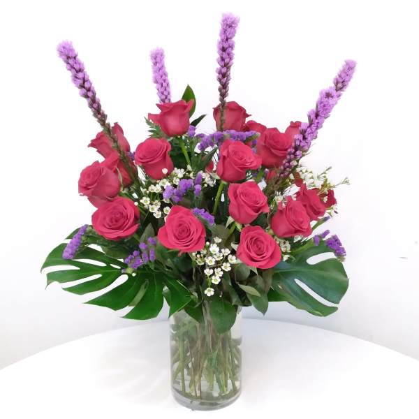 Pink roses in a clear glass vase with purple spikes and tropical leaves