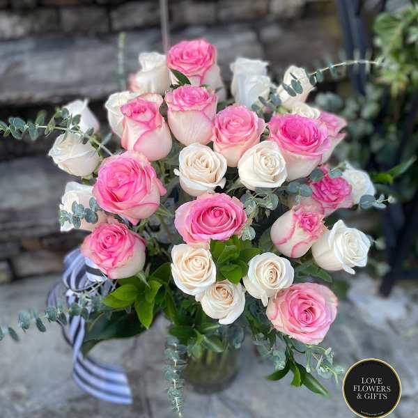 Arrangement of pink and white roses in a clear glass vase with striped ribbon