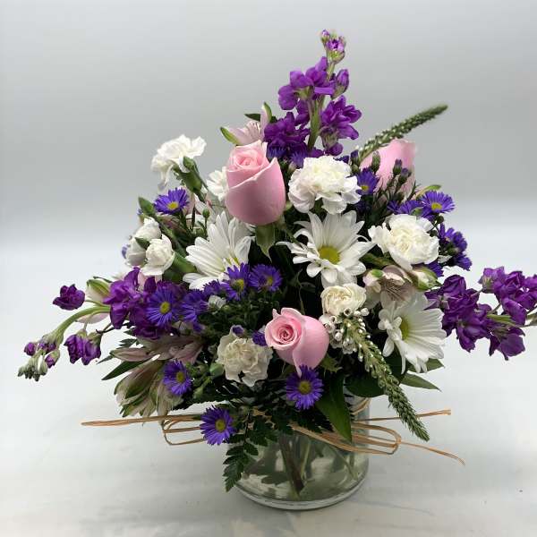 Mixed bouquet of pink roses, white daisies, and purple flowers in a glass vase