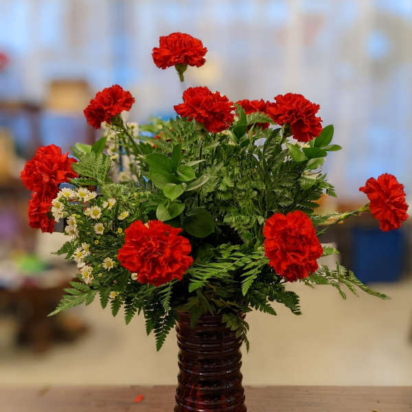 Red carnations arranged in a red glass vase with mixed greenery