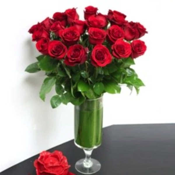 Red roses arranged in a tall glass vase with greenery