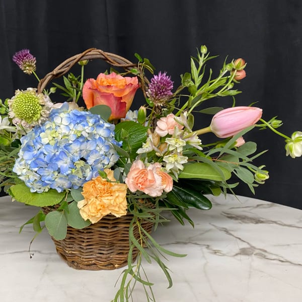 Basket arrangement with blue hydrangea, roses, tulips, and carnations