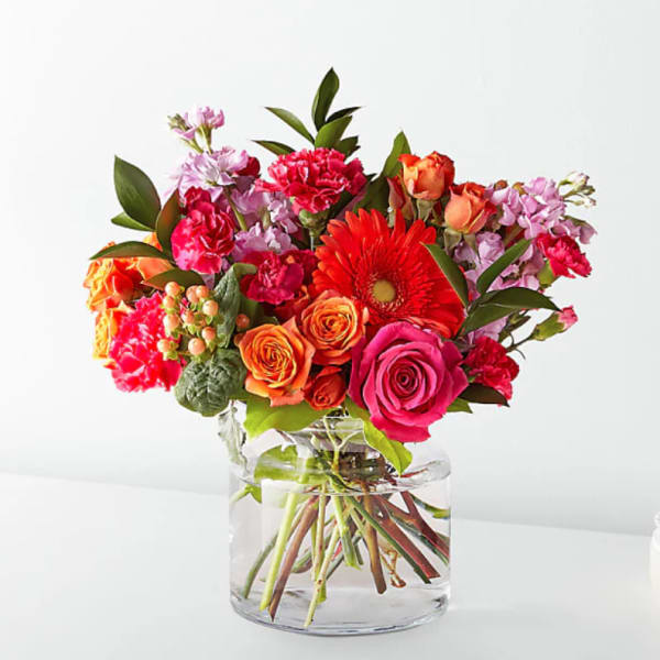 Bright mixed bouquet of roses, gerbera daisies, and carnations in a clear glass vase