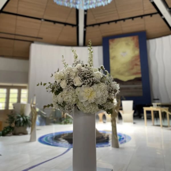 White floral arrangement on a tall pedestal in a ceremony space