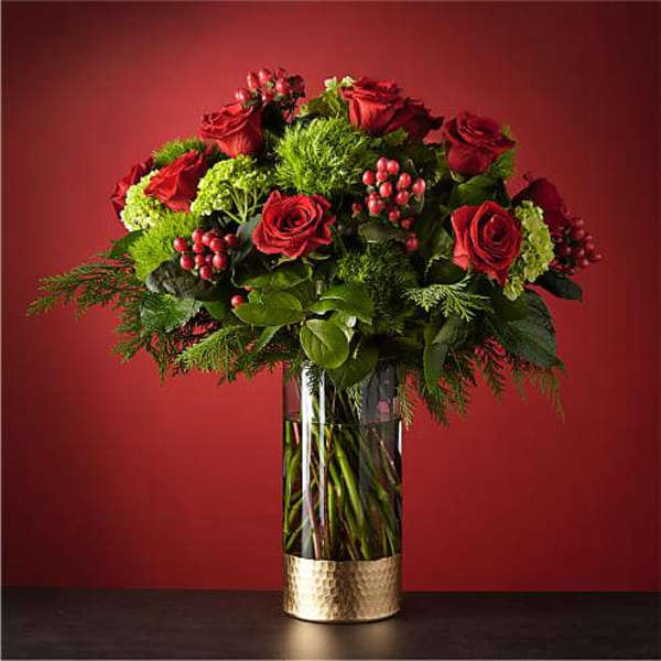 Red roses arranged in a tall glass vase with greenery