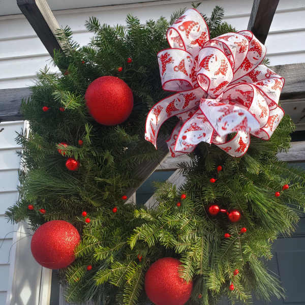 Christmas wreath with red ornaments and a white ribbon bow