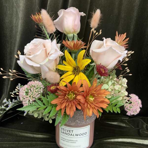 Mixed floral arrangement in a pink candle jar with pale roses and orange daisies