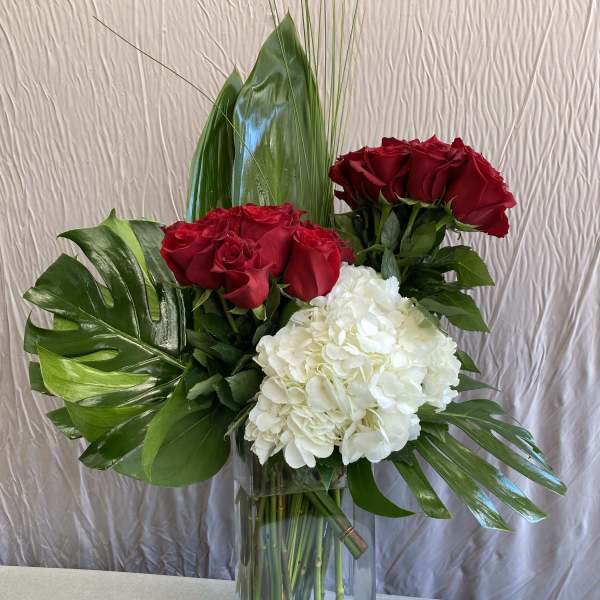 Red roses and white hydrangea in a clear glass vase with tropical leaves