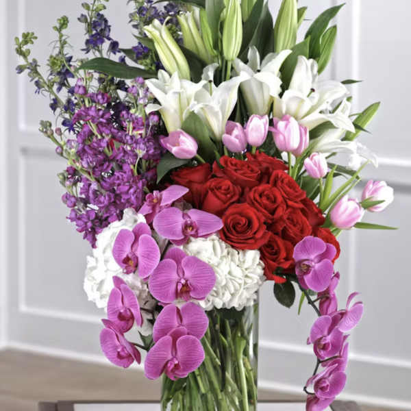 Tall bouquet of red roses, white lilies, pink tulips, and purple orchids in a glass vase