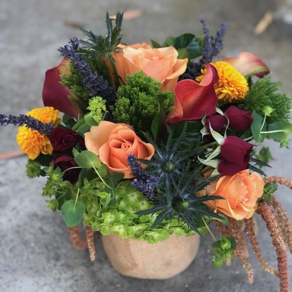 Mixed bouquet with peach roses, burgundy calla lilies, and yellow blooms in a burlap pot