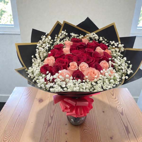 Bouquet of red and blush roses with white baby's breath in black wrap