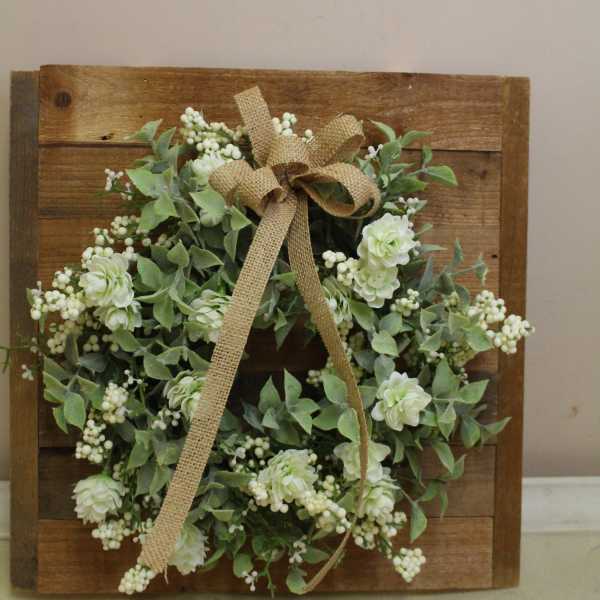 White floral wreath with a burlap bow on a wooden board