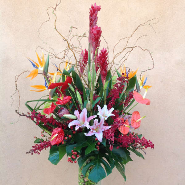 Tall tropical flower arrangement in a clear glass vase with pink lilies and bird of paradise