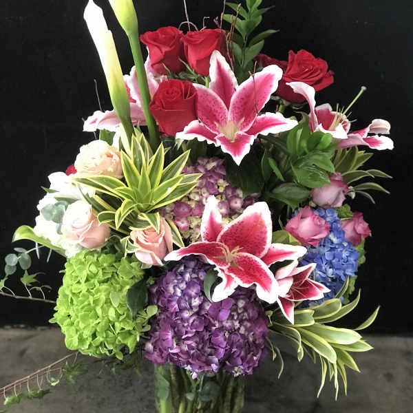 Mixed bouquet with red roses, pink lilies, and hydrangeas in a glass vase