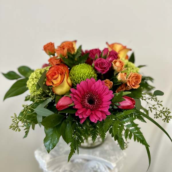Bright mixed bouquet with pink gerbera, roses, and green mums in a glass vase