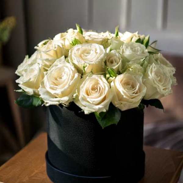 Cream roses arranged in a black hatbox