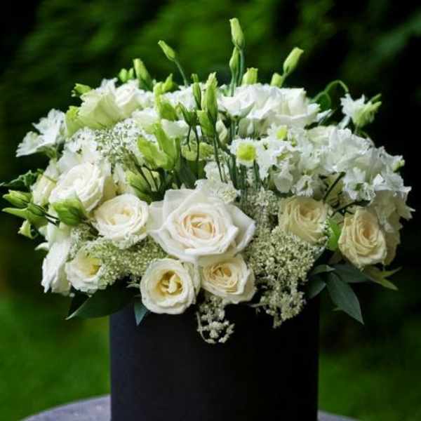 White roses and white blooms arranged in a black hatbox