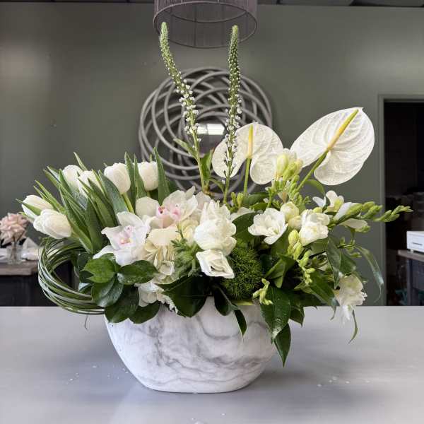 White floral arrangement in a marble-look bowl with tall stems and orchids