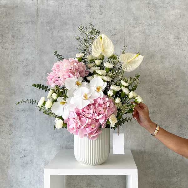 Pink hydrangeas and white orchids arranged in a white vase