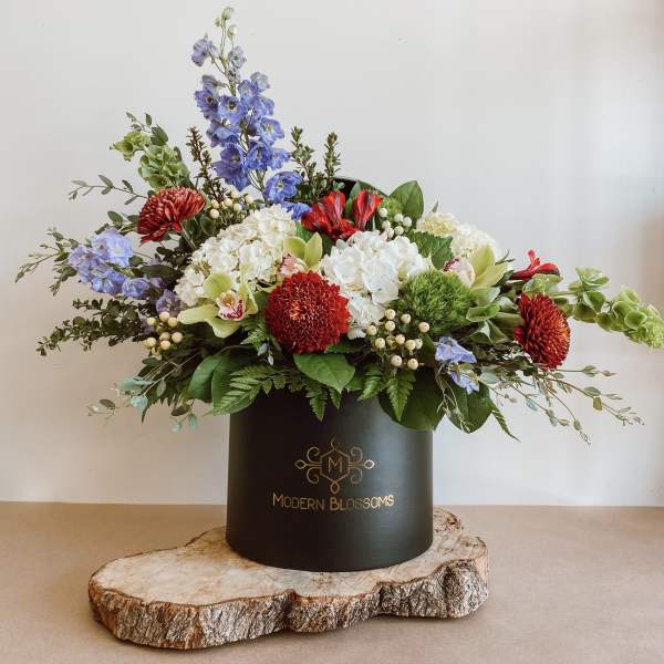 Mixed floral arrangement in a black hatbox with red, white, blue, and green blooms