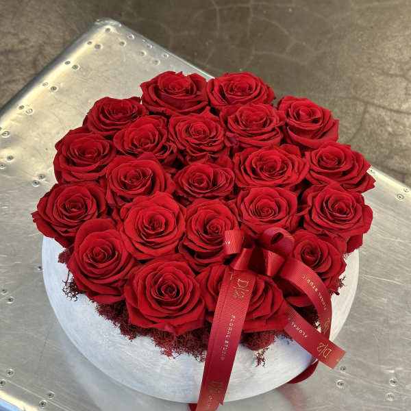 Round arrangement of red roses in a white hat box with a red ribbon
