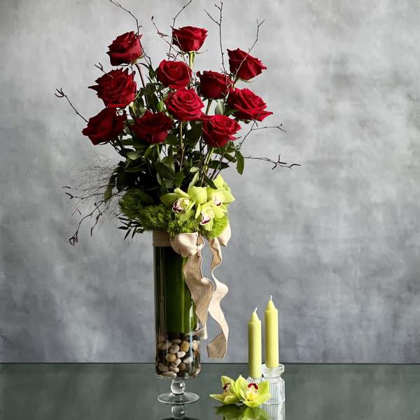Tall bouquet of red roses and green orchids in a glass vase