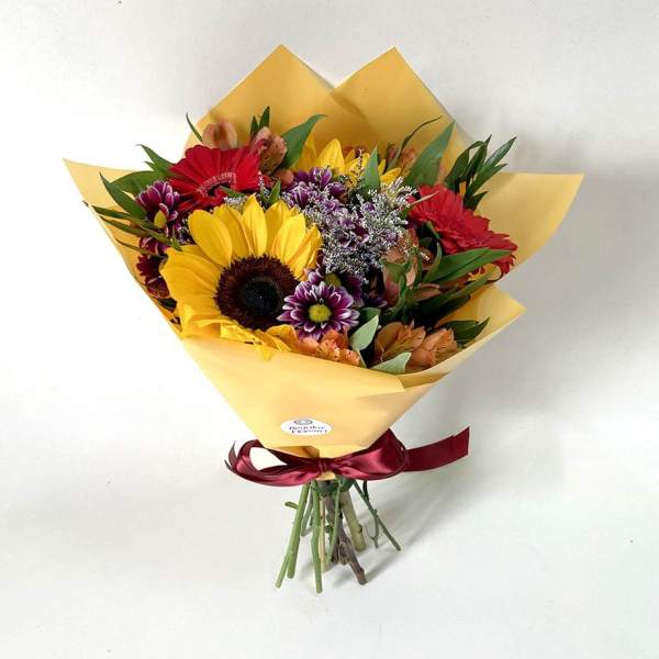 Mixed bouquet with a sunflower, red gerberas, and purple flowers in yellow wrap