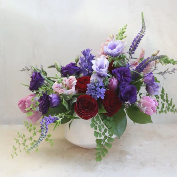 Mixed bouquet of red, pink, and purple flowers in a white vase