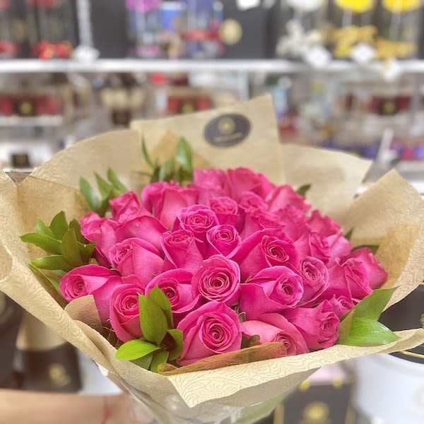 Bouquet of bright pink roses wrapped in tan patterned paper with a black ribbon tie.