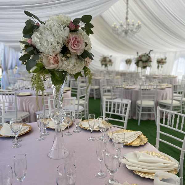 Tall floral centerpiece with white hydrangeas and pale pink roses in a clear vase