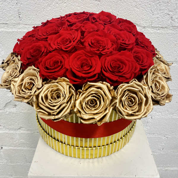 Round arrangement of red and gold roses in a striped box
