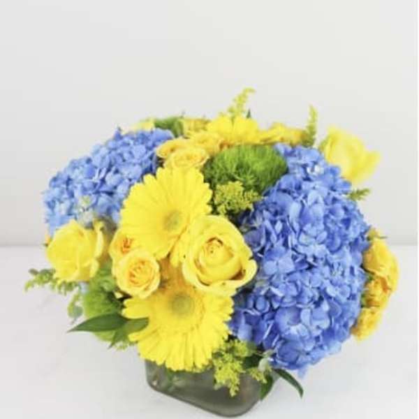 Blue hydrangeas and yellow roses in a square glass vase