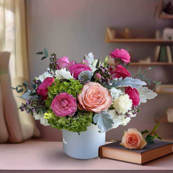 Mixed pink and white flower arrangement in a white vase with a rose on a book