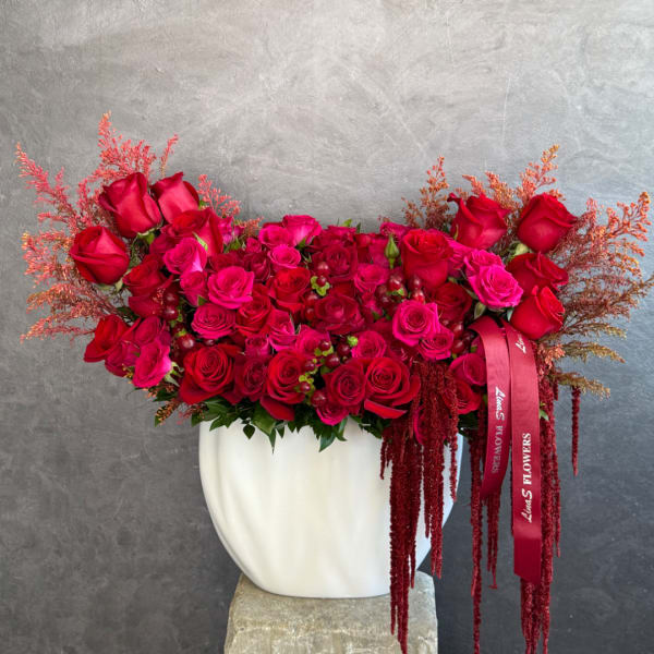 Red and pink rose arrangement in a white vase with ribbon accents