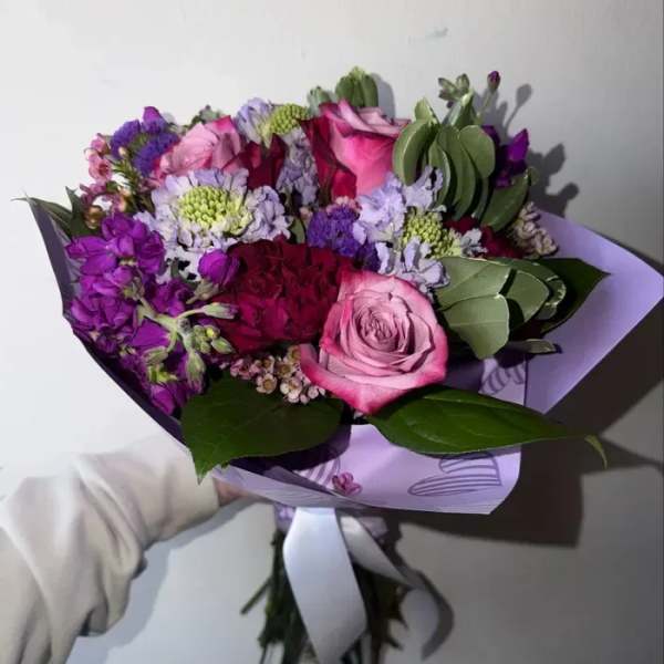 Handheld bouquet of pink and purple flowers wrapped in lavender paper