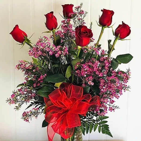 Red roses and pink filler flowers in a glass vase with a red bow