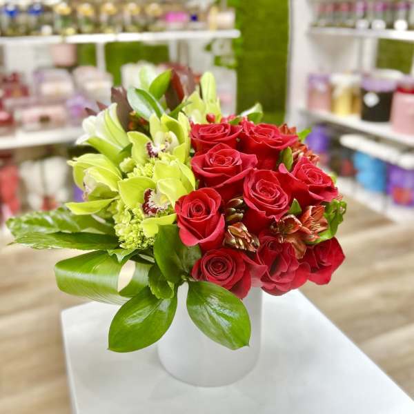 Arrangement of red roses and green orchids in a white cylinder vase