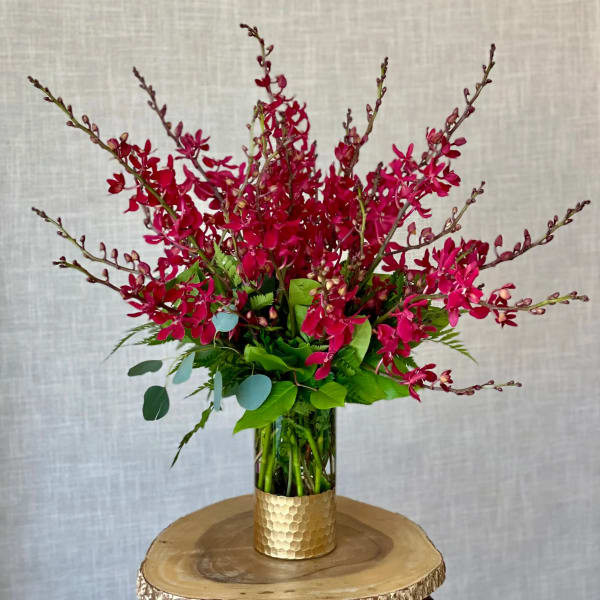 Magenta orchid arrangement in a gold vase on a wood slice