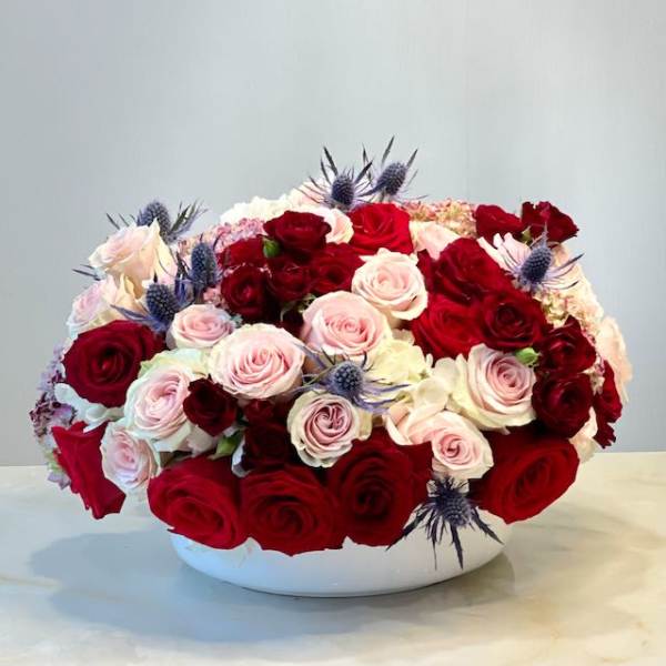 Red and blush roses arranged in a white bowl vase