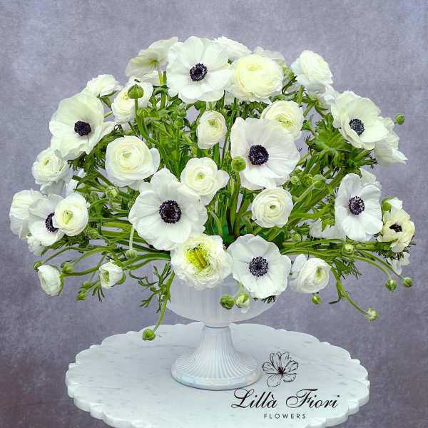 White anemones and ranunculus arranged in a white pedestal vase
