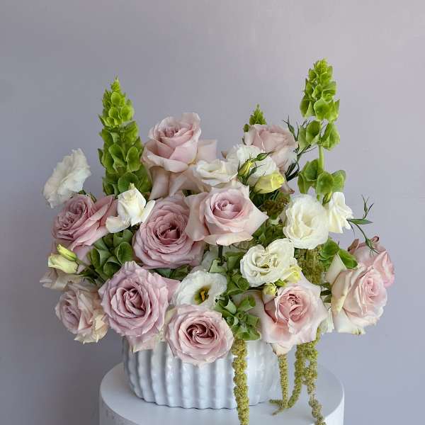 Pink and white roses arranged in a white vase with green spikes
